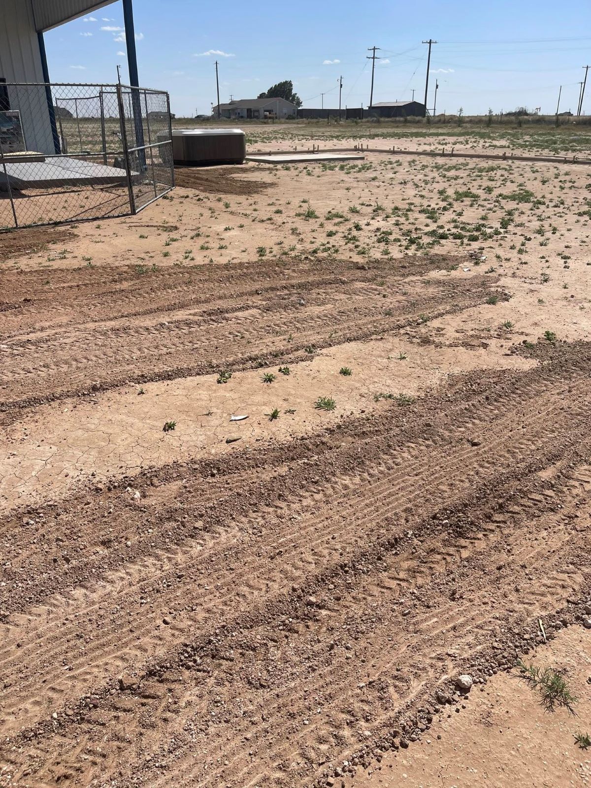 Tire tracks in dirt field near a building, on a sunny day.