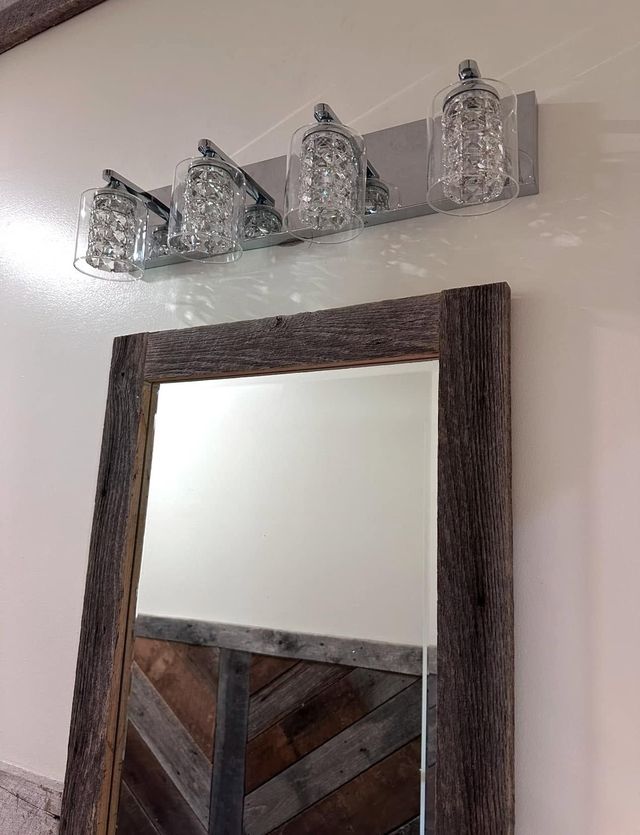 Four small silver birdhouse decorations above a rustic wood-framed mirror on a light wall