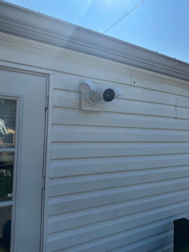 White house siding with a small security camera mounted near a door under the eaves