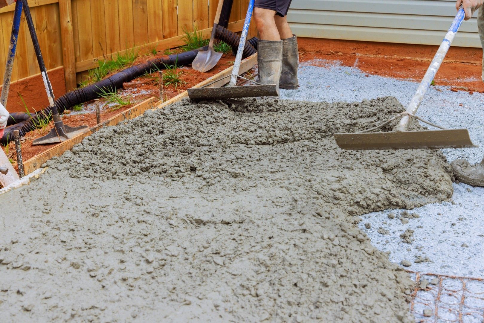 Workers spreading wet concrete with long-handled floats on a prepared surface, outdoor construction.