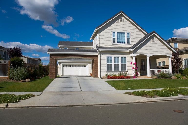 Two-story beige house with a white garage, green lawn, and blue sky.