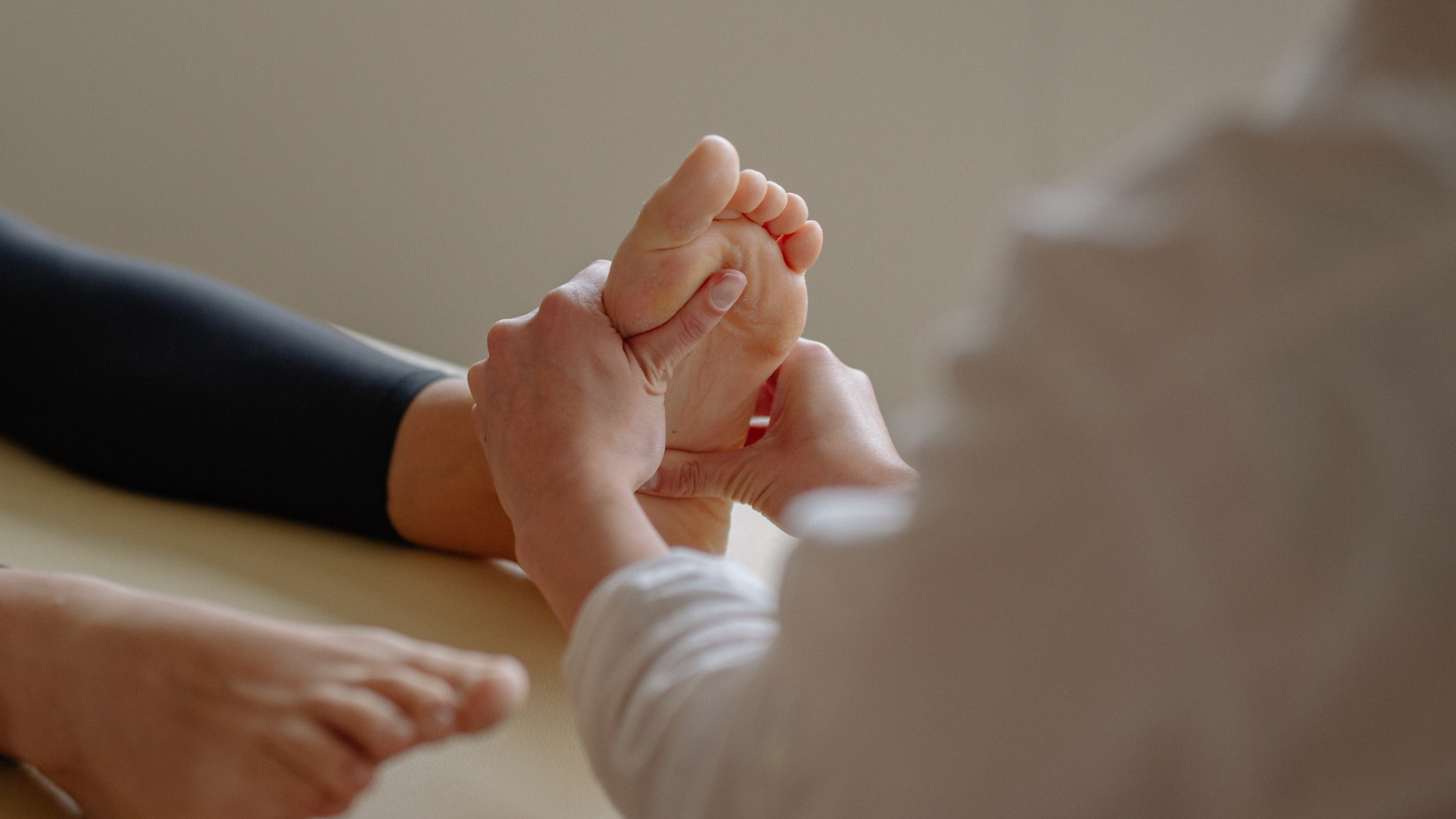 Person receiving a foot massage. The masseuse’s hands are on the sole of a foot, with the other foot visible.