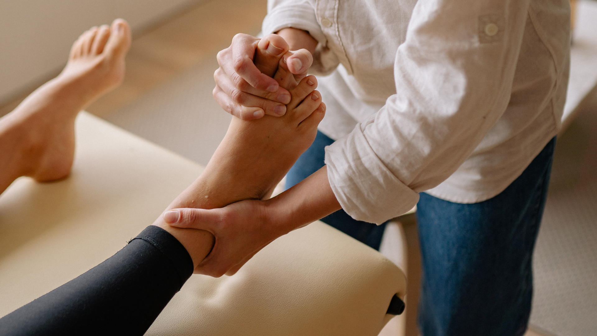A person's foot and ankle being massaged on a massage table by a person wearing a white shirt and jeans.