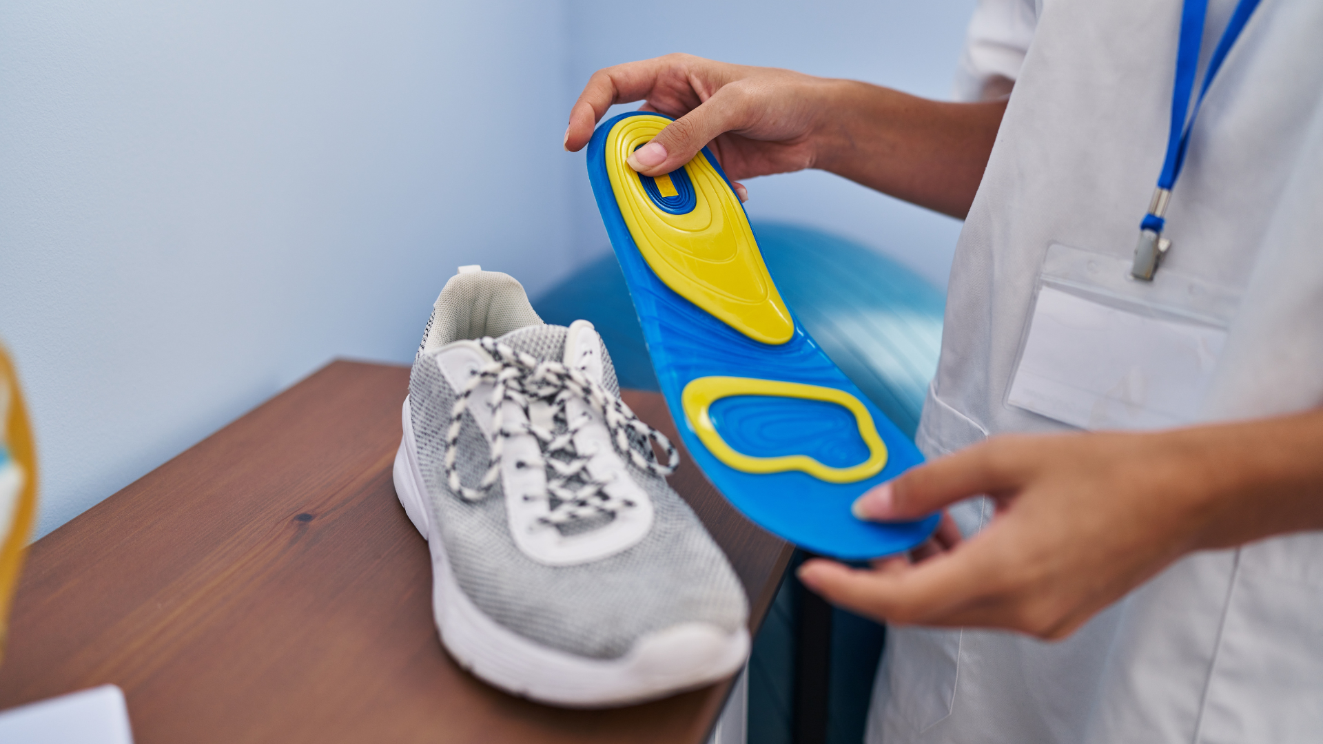 Person holding a blue and yellow insole next to a gray sneaker. The insole is likely for orthotics.