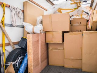 Inside of a moving truck packed with cardboard boxes, a spare tire, and furniture wrapped in protective material.