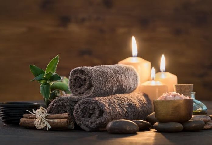 A stack of towels , candles , cinnamon sticks and rocks on a table.