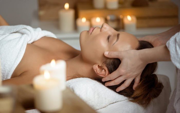 A woman is getting a head massage in a spa with candles in the background.