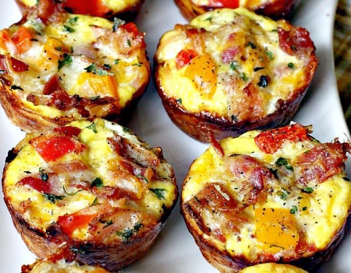 A white plate topped with mini quiches with bacon and tomatoes