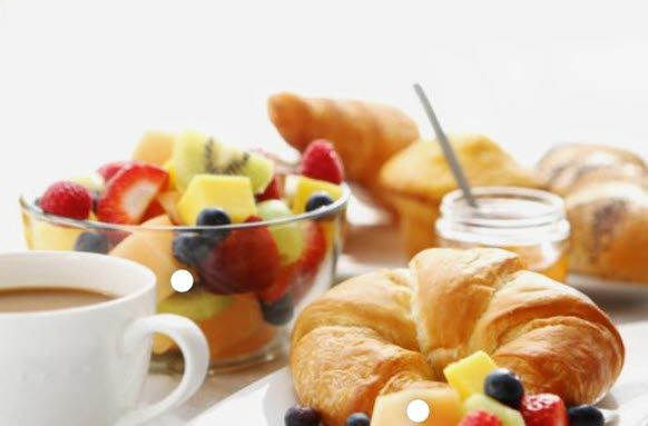 A table topped with a cup of coffee , croissants , fruit and a bowl of fruit.
