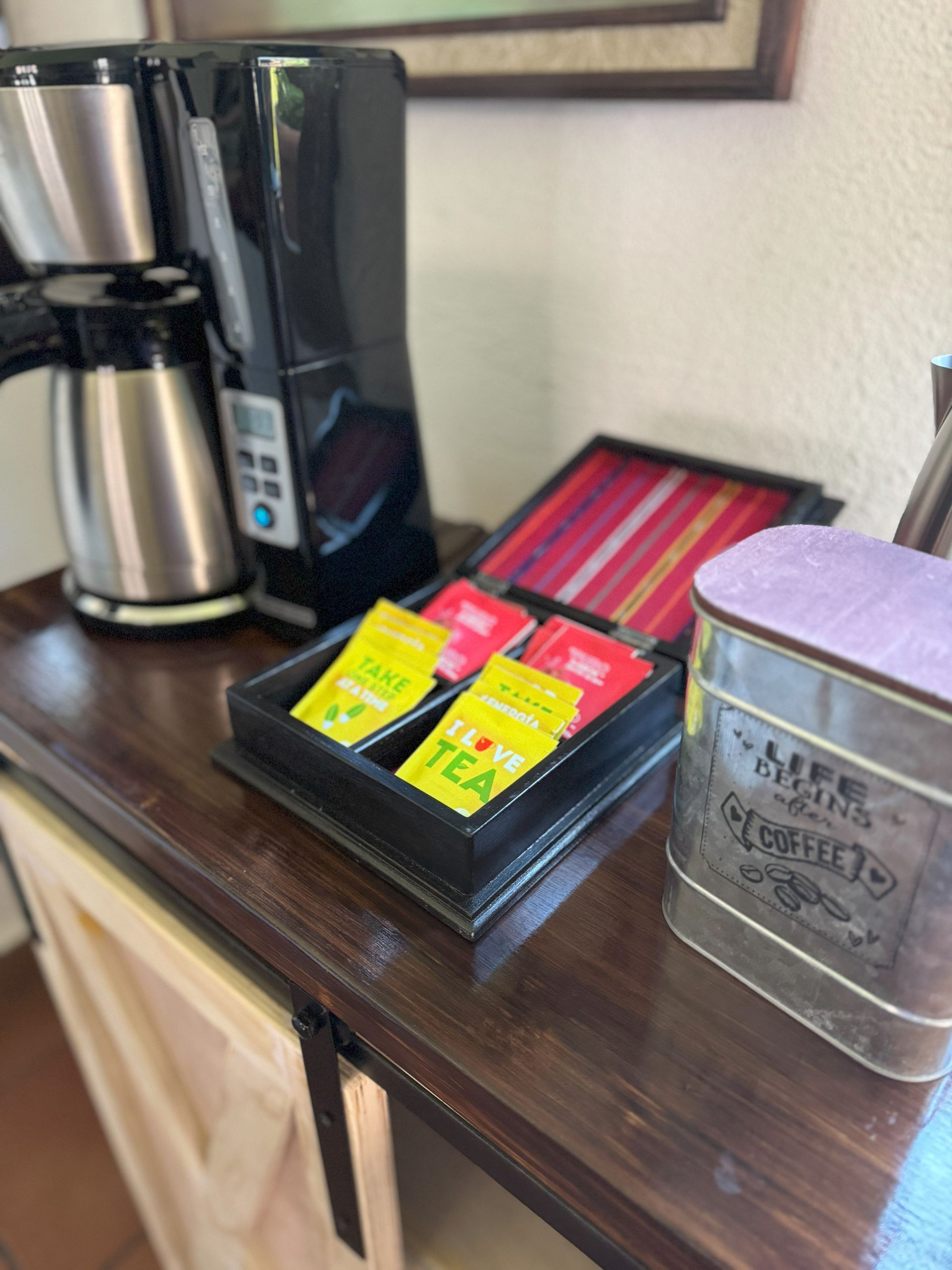 A coffee maker is sitting on a wooden counter next to a tray of tea bags.
