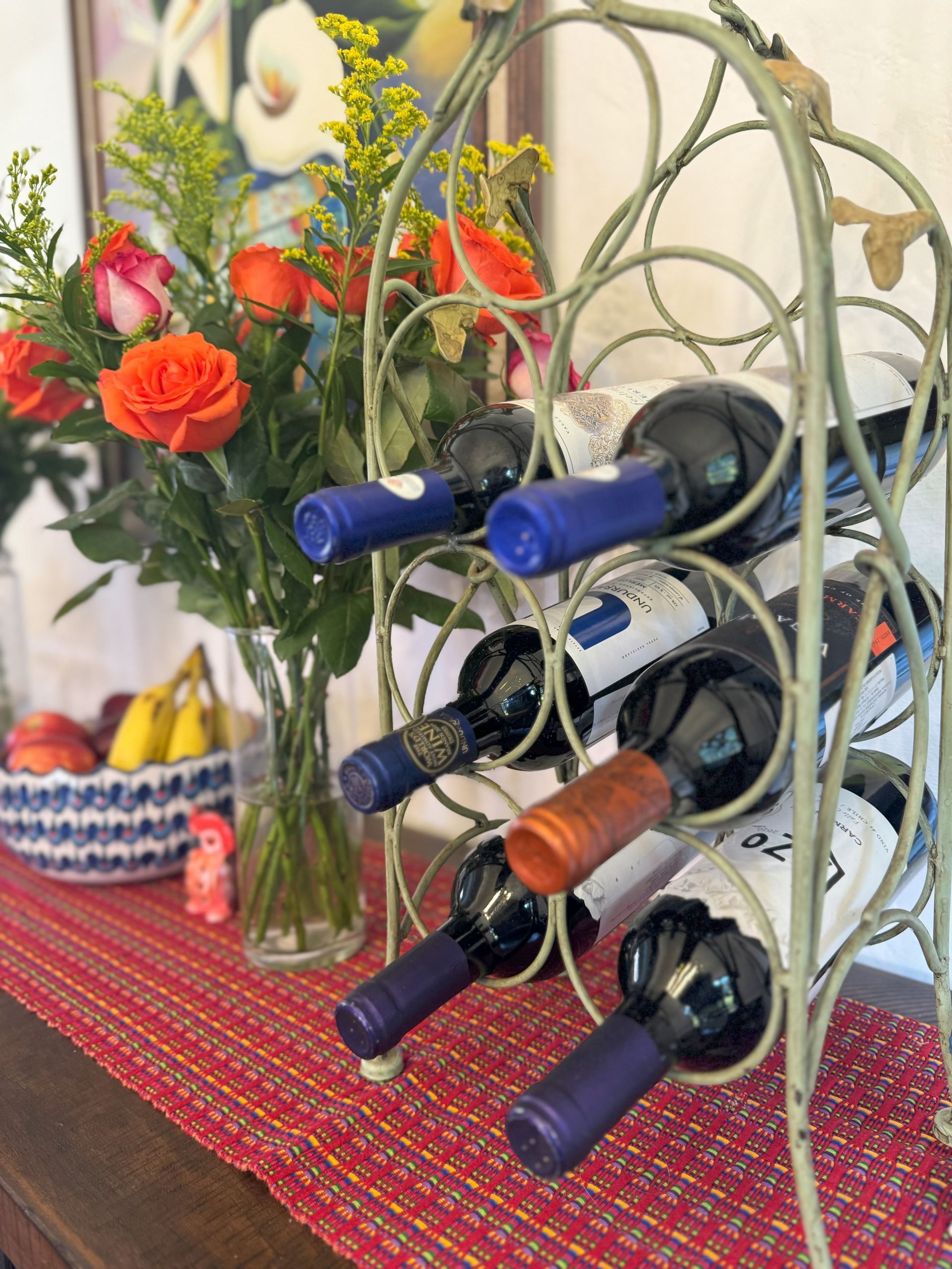 A wine rack filled with wine bottles is on a table next to a vase of flowers.