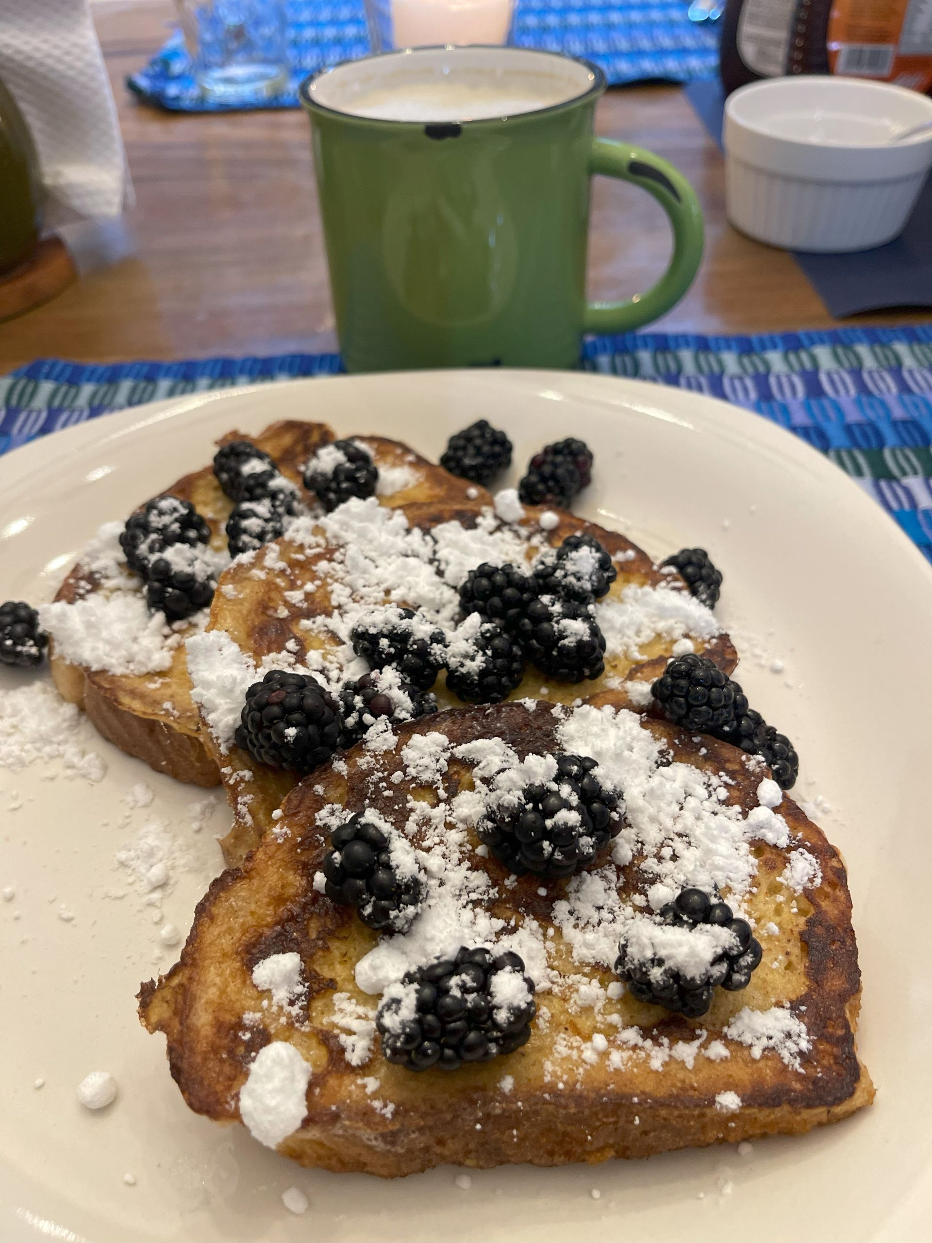 A plate of french toast with blackberries and powdered sugar next to a cup of milk.
