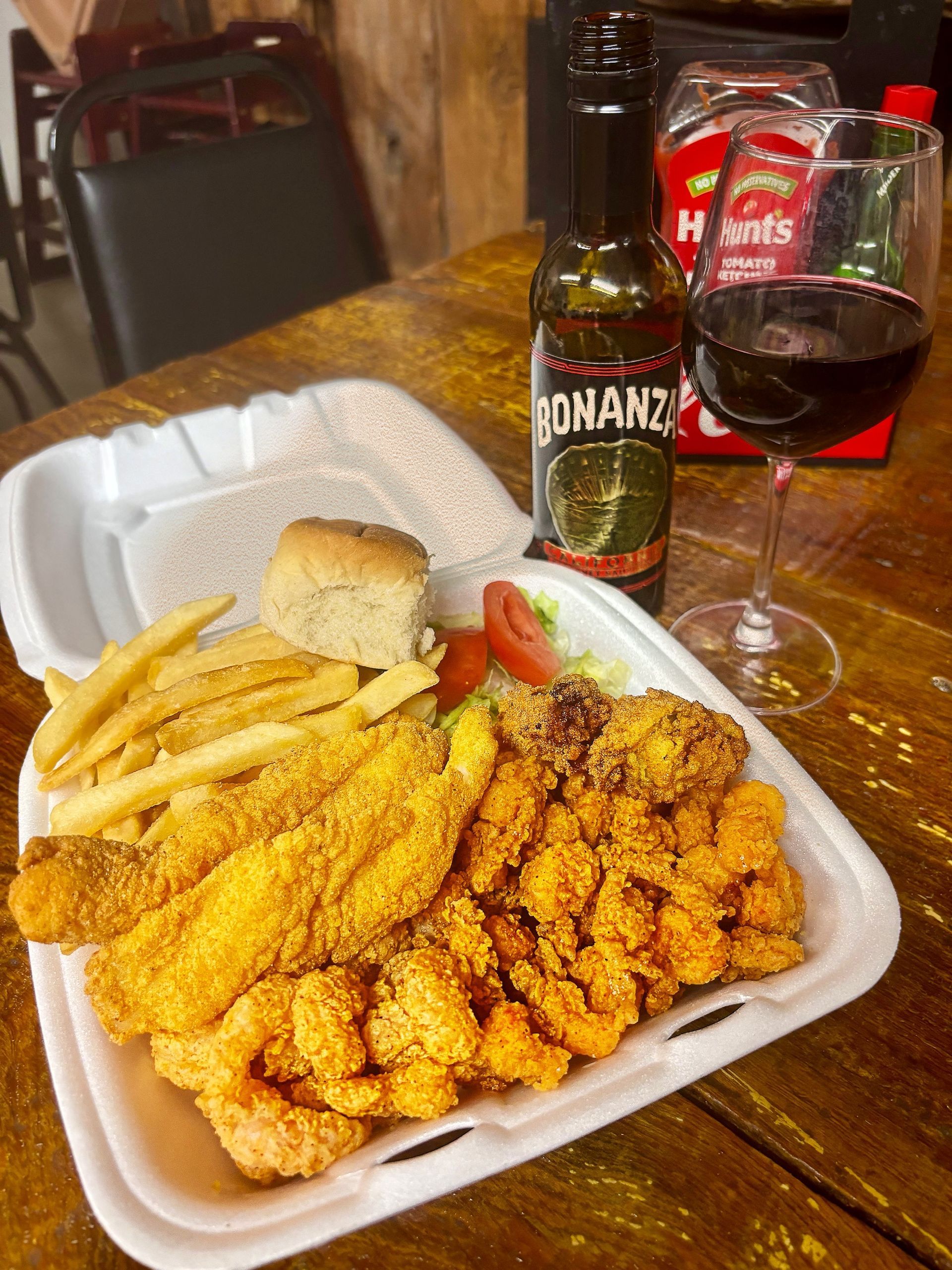 Fried fish and shrimp platter with fries, roll, and wine on a table.