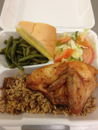 Chicken dinner in a white foam container with rice, beans, salad, and bread.