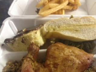 Meal in a white takeout container with chicken, cornbread, fries, and bread.