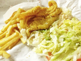 Fried fish sandwich with fries and coleslaw on paper.
