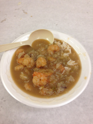 Shrimp stew with rice in a white bowl with a white plastic spoon.