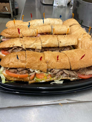 Large platter of sliced sandwiches with toothpicks, containing meat, lettuce, and tomatoes.