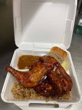 Half roasted chicken with rice, beans, a roll, and slaw in a takeout container.