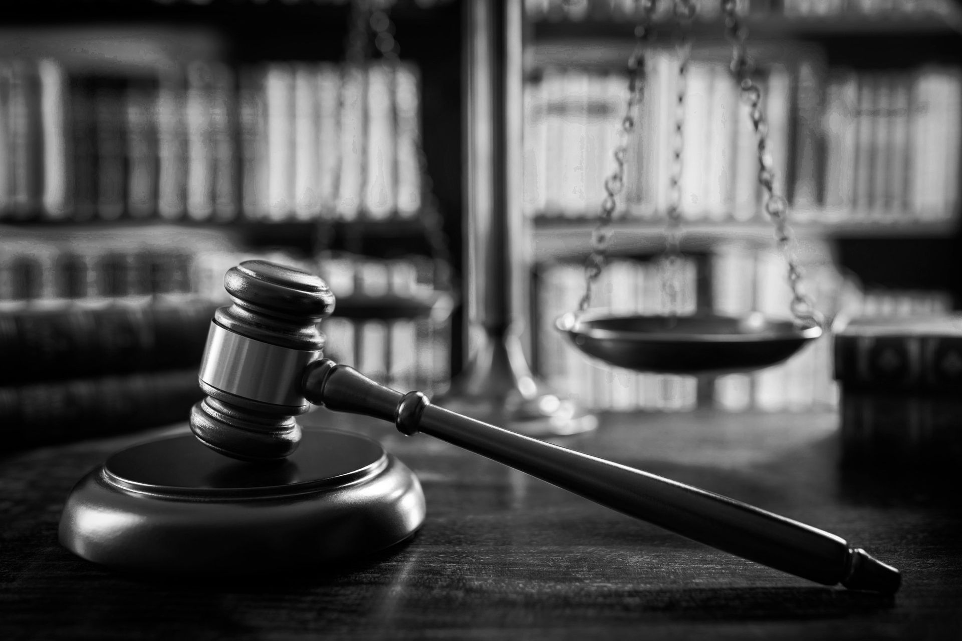 Gavel on a wooden block, scales of justice in background, in front of a bookcase.