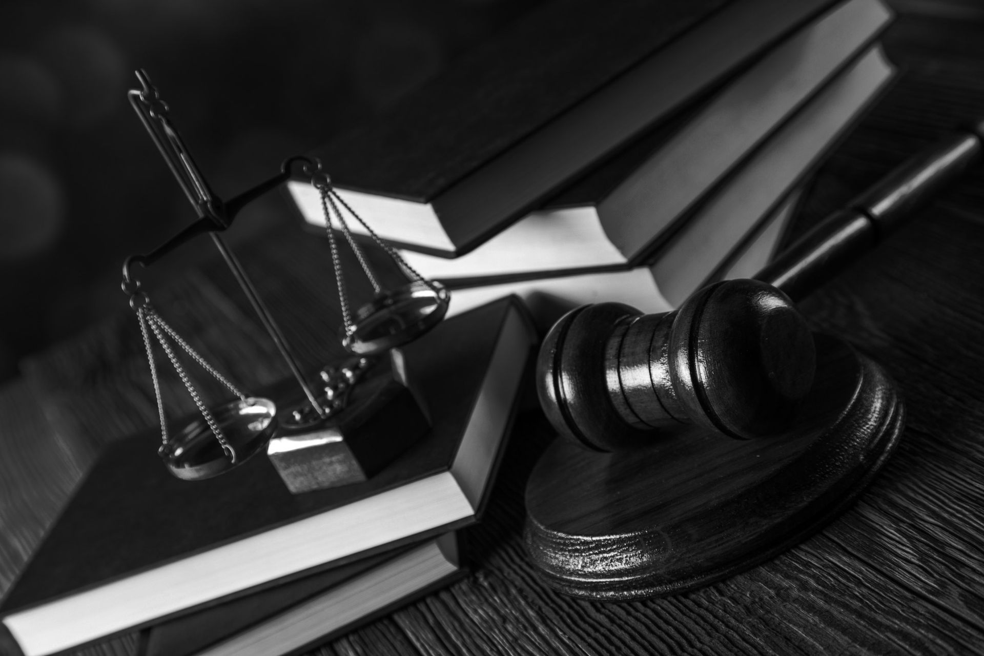 Scales of justice, gavel, and books on a wooden surface, black and white.