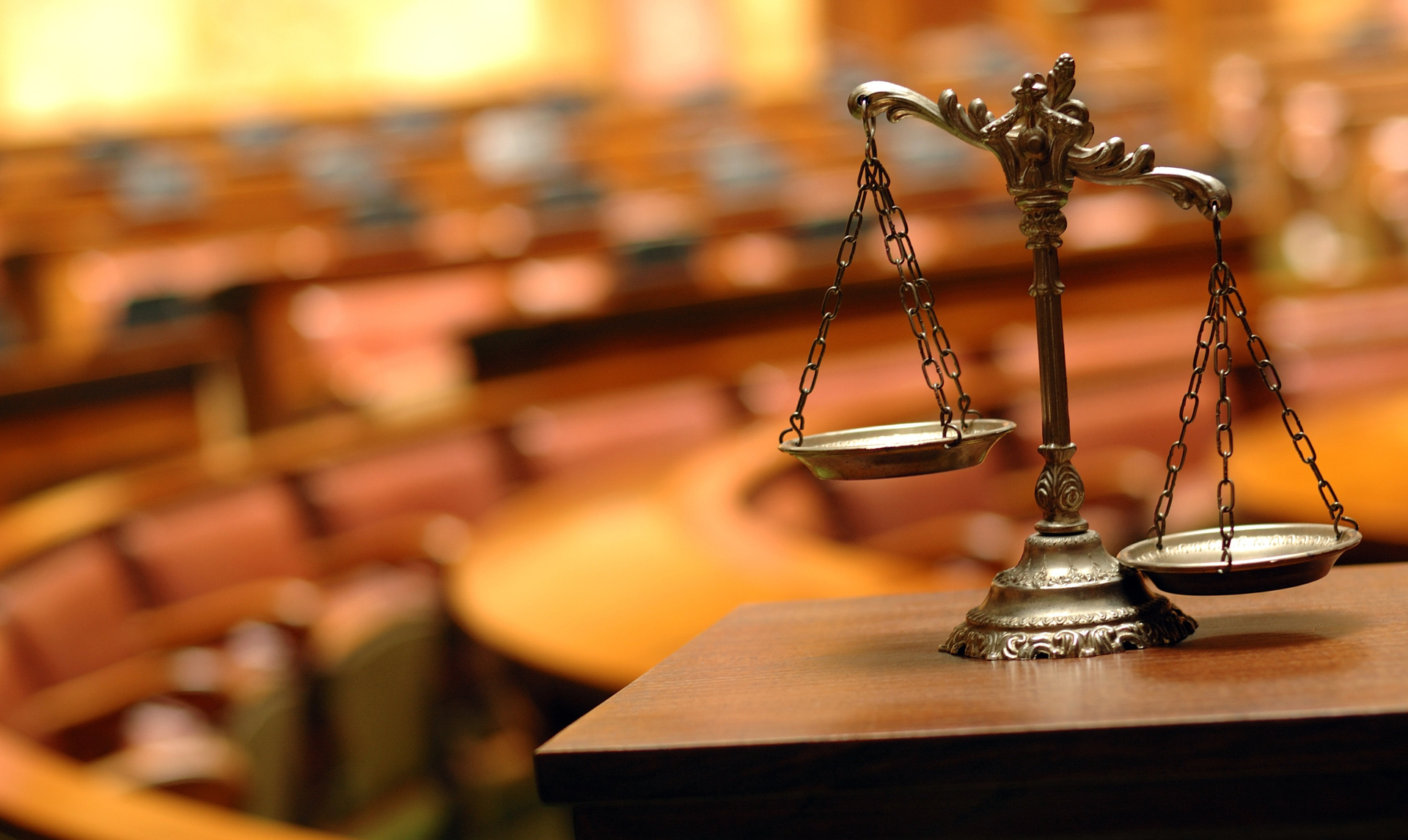 Scales of justice on a wooden table in a courtroom.