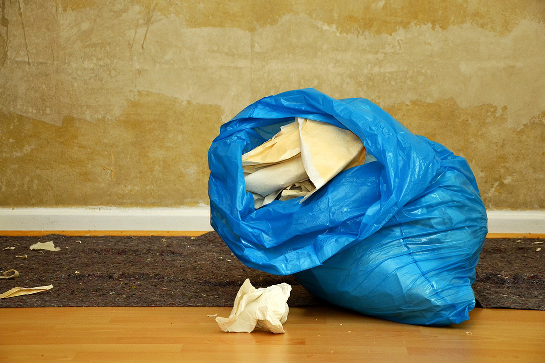 Blue trash bag overflowing with debris, next to a damaged wall.