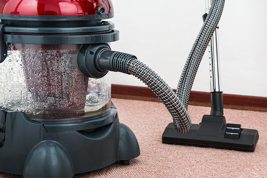 Red and black vacuum cleaner with transparent container, vacuuming a carpet.