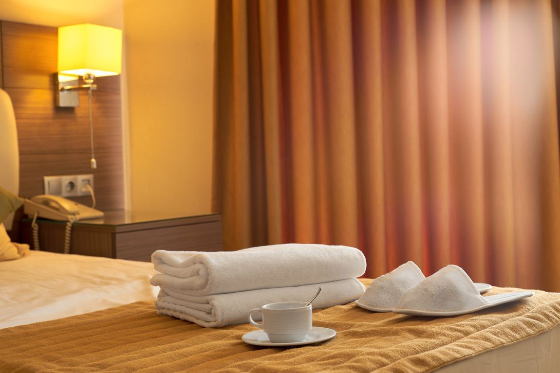 Camera di hotel con tazza, pantofole e asciugamani sul letto