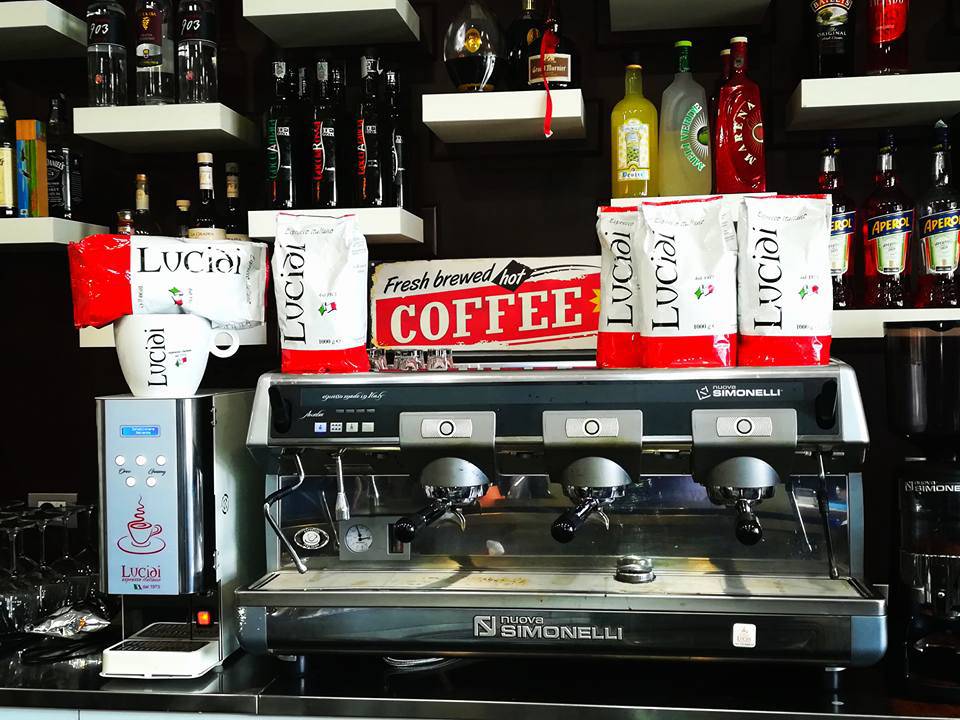 Una macchina da caffè, una tazza e alcune confezioni da caffè macinato Lucidi Espresso Italiano