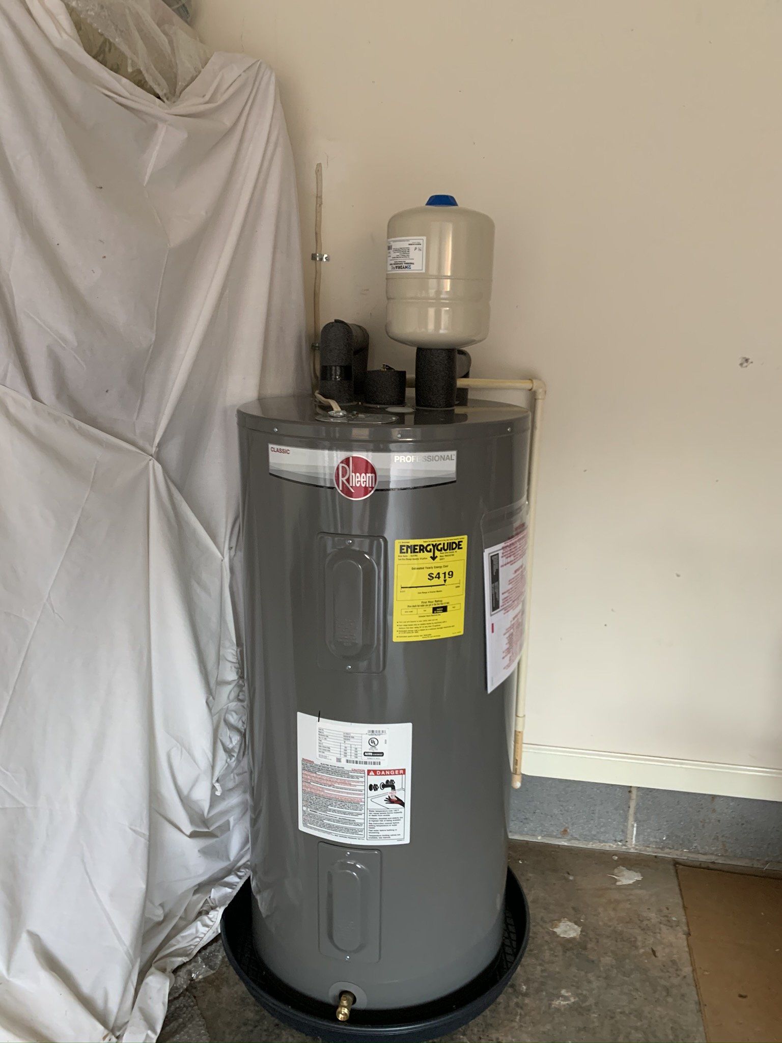 A gray water heater is sitting in a garage next to a wall.