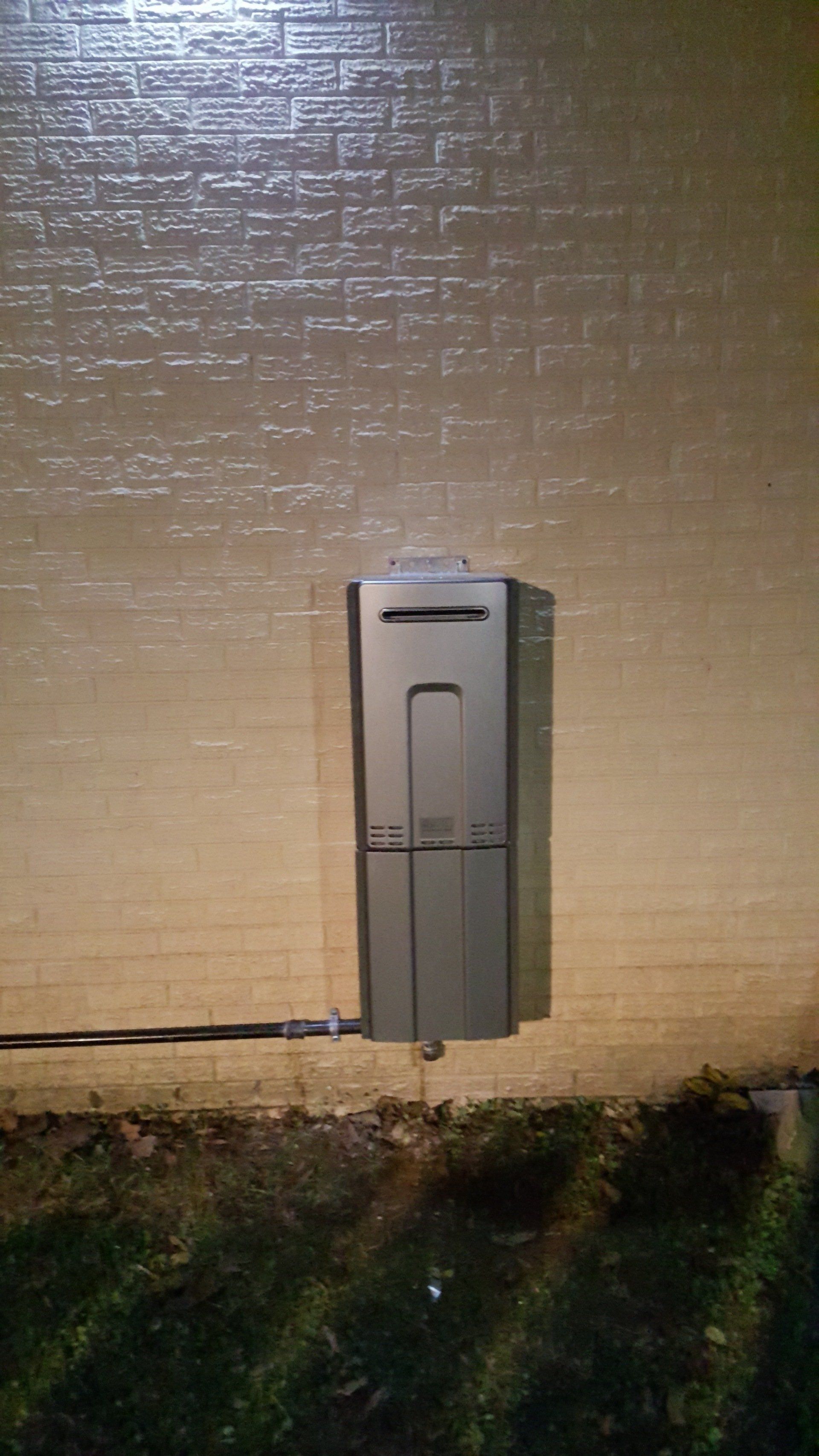 A water heater is attached to the side of a brick building.