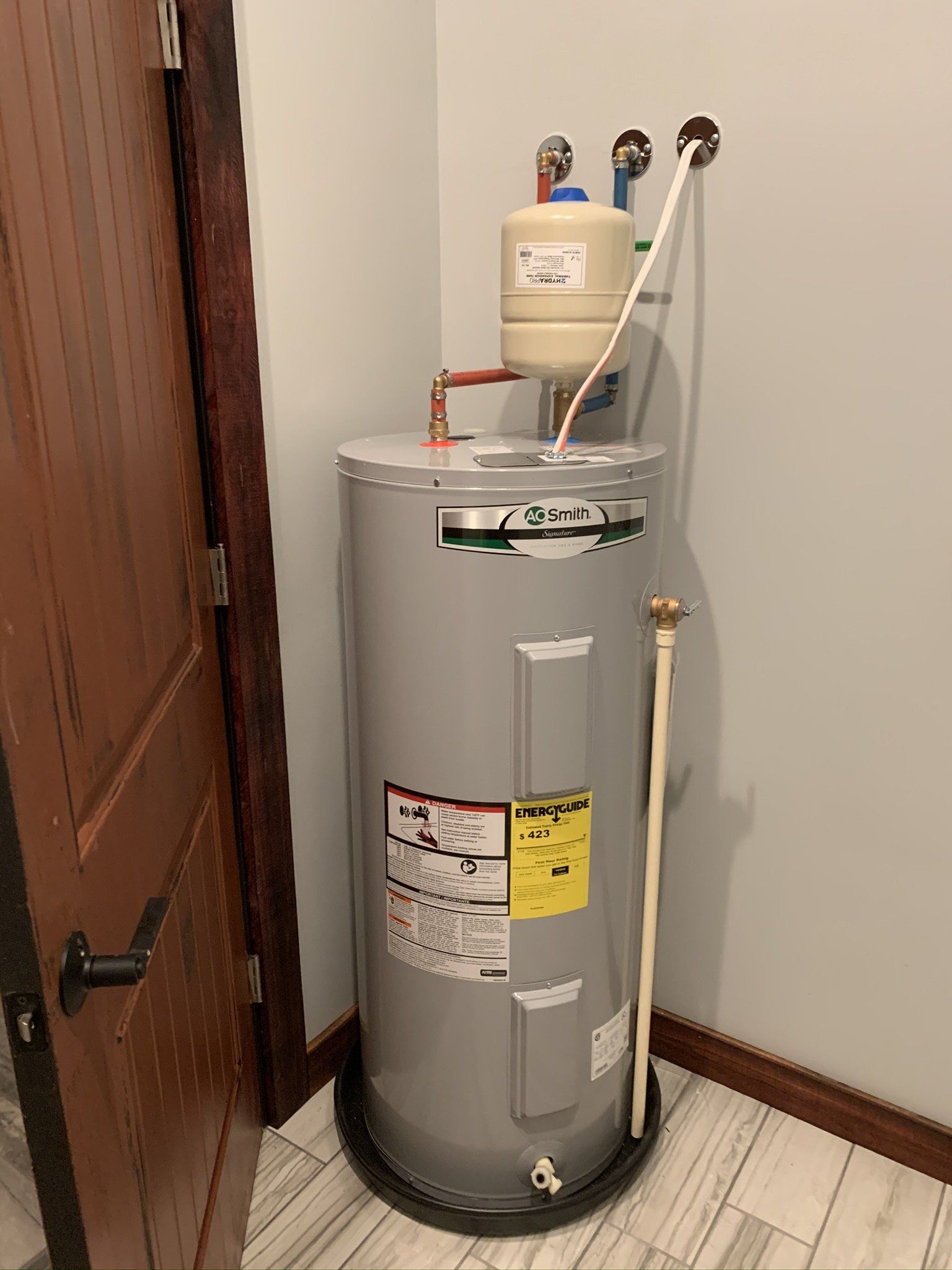 A water heater is sitting in a corner of a room next to a door.
