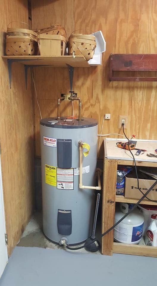 A water heater is sitting in a room next to a wooden cabinet.