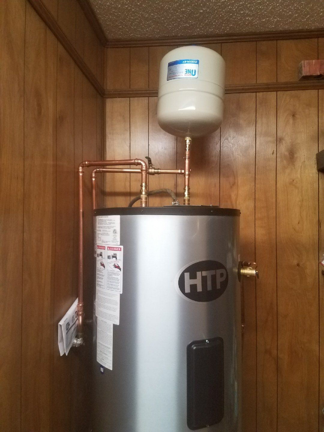 A water heater is mounted to a wooden wall in a room.