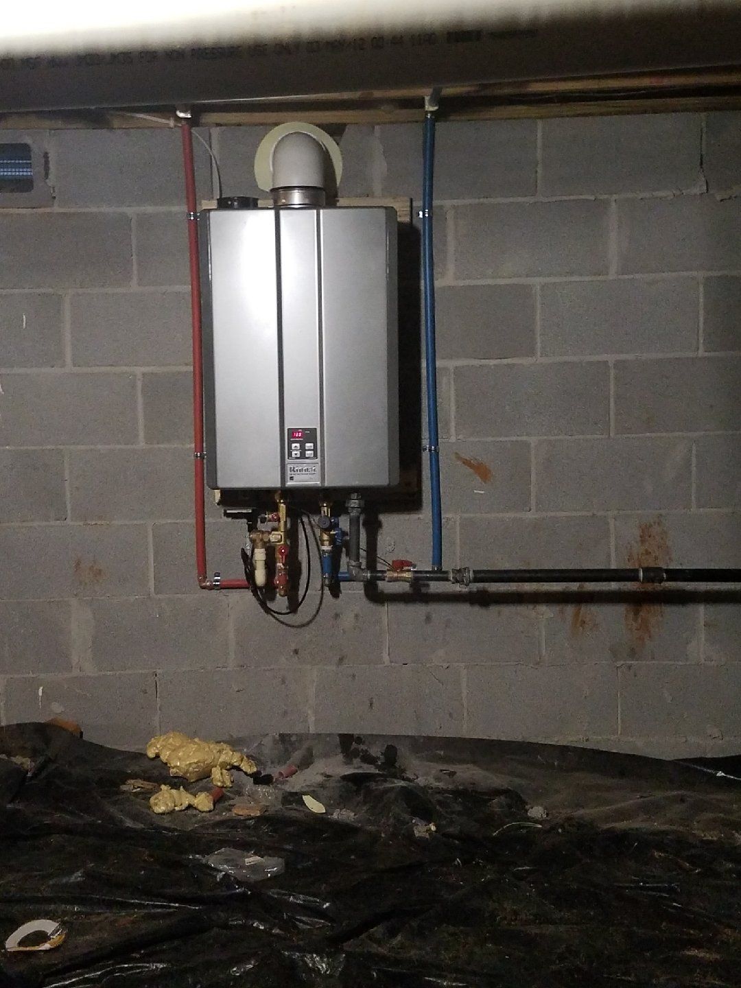 A water heater is mounted to a brick wall in a basement