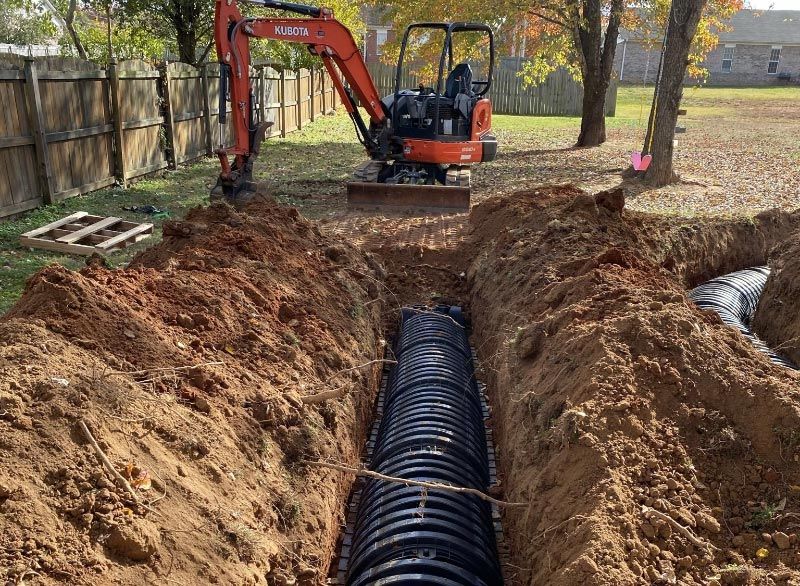 J Henry Plumbing operating an excavator is digging a hole in the ground to install a septic tank .