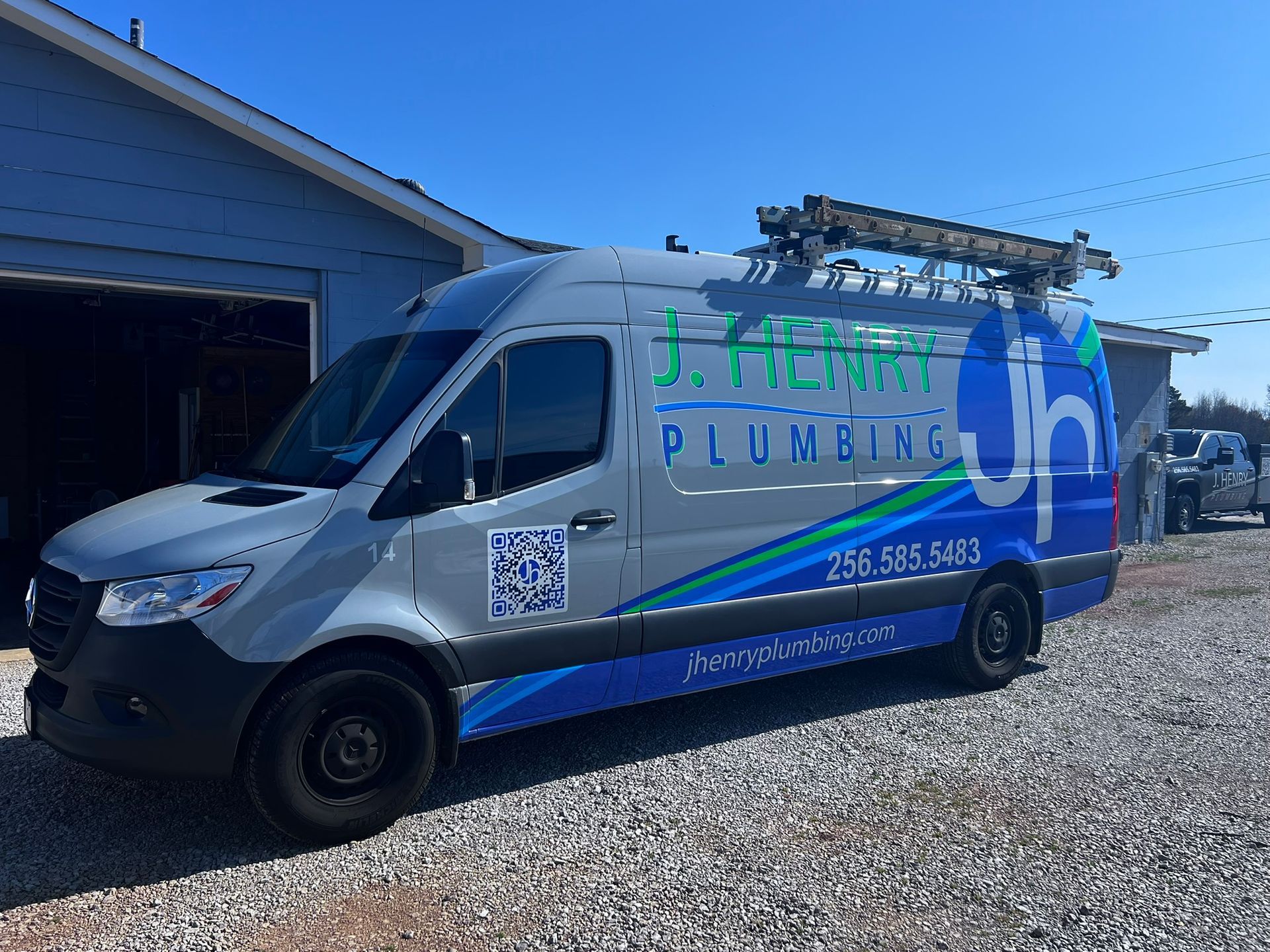 A j. henry plumbing van is parked in a gravel lot.