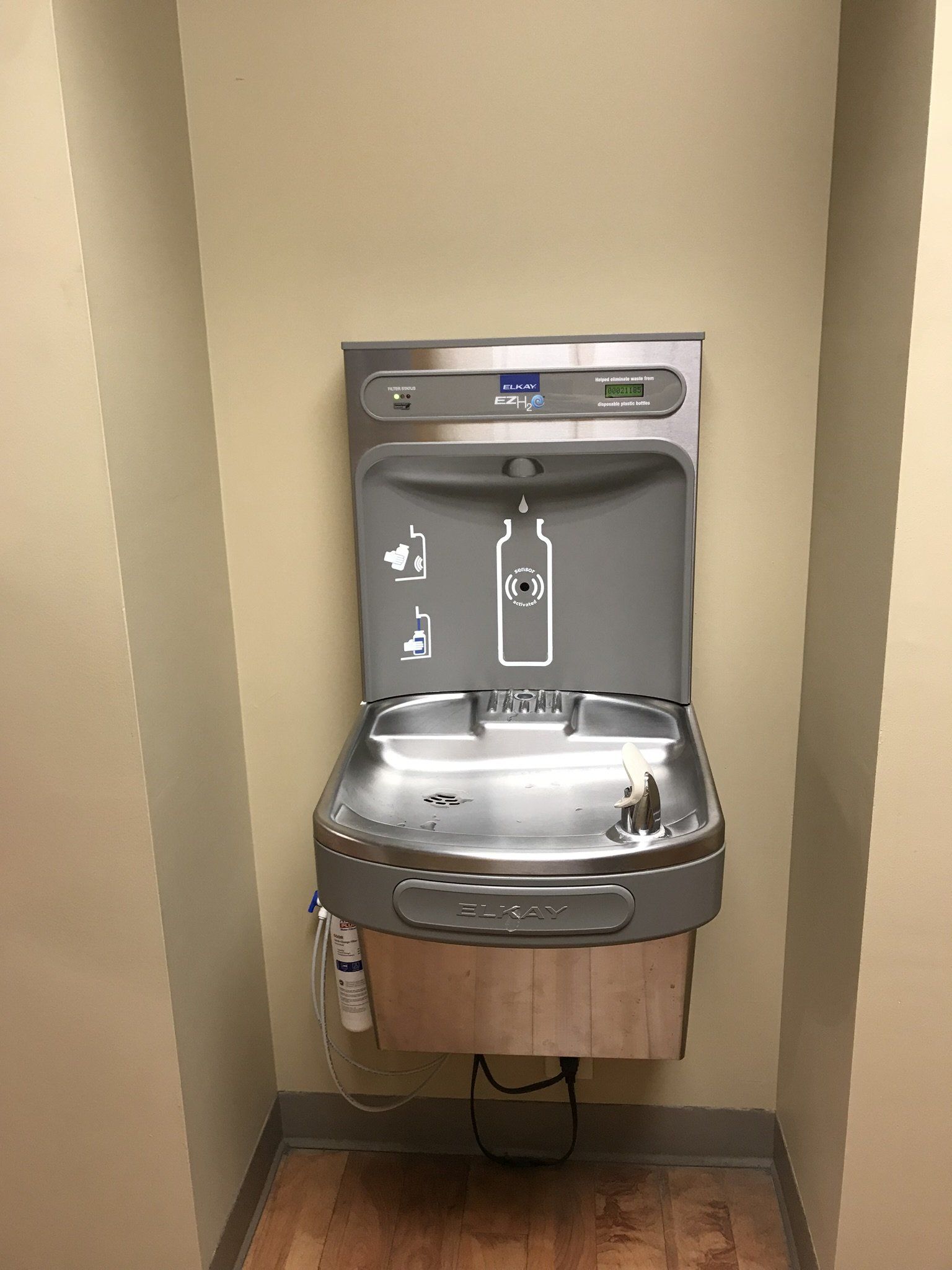 A stainless steel water fountain is hanging on a wall in a bathroom.