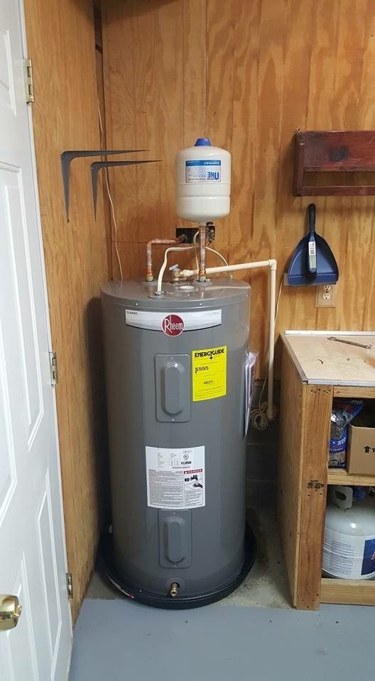 A gray water heater is sitting in a room next to a wooden wall.