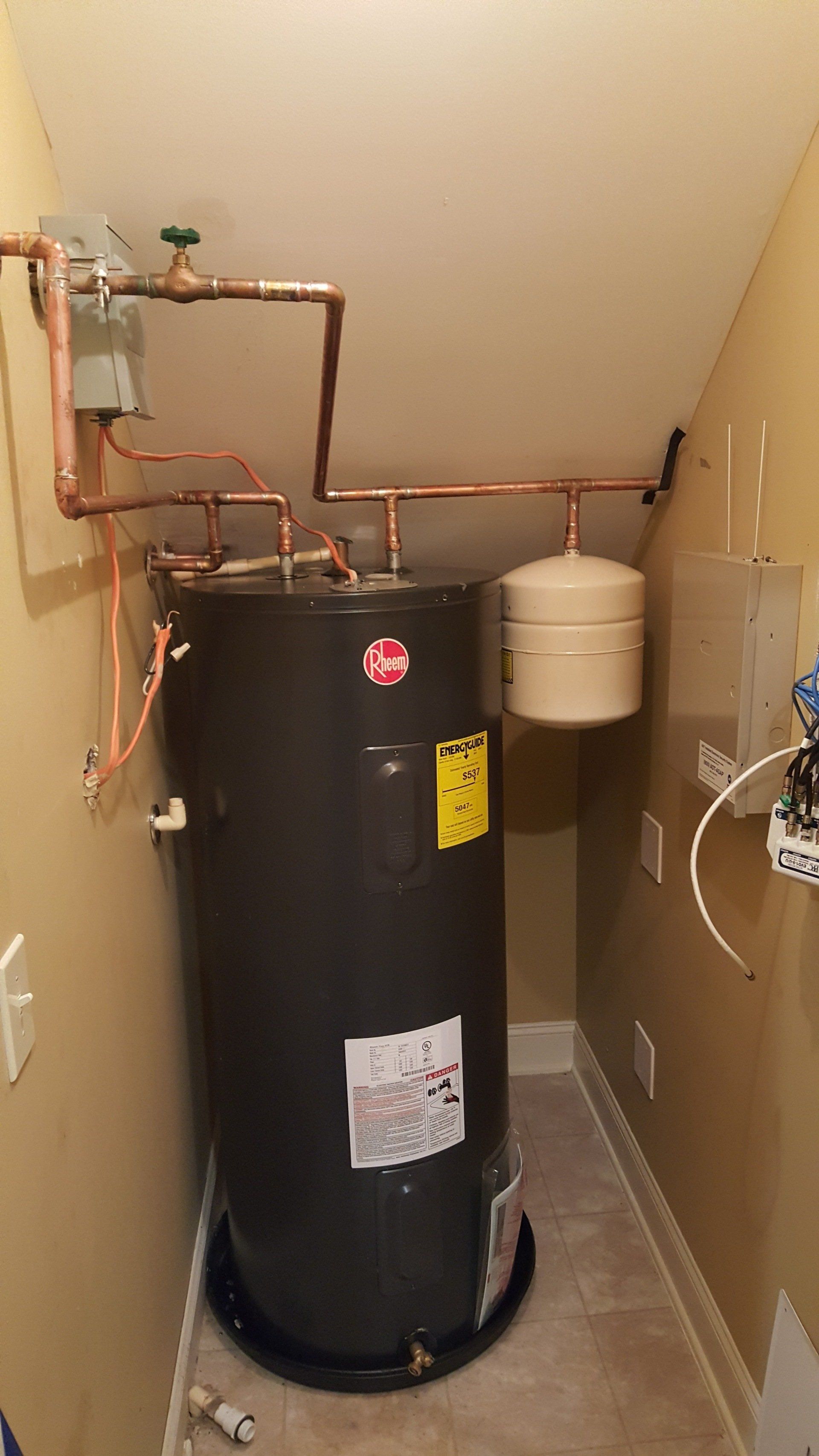 A water heater is sitting in a hallway under a staircase.