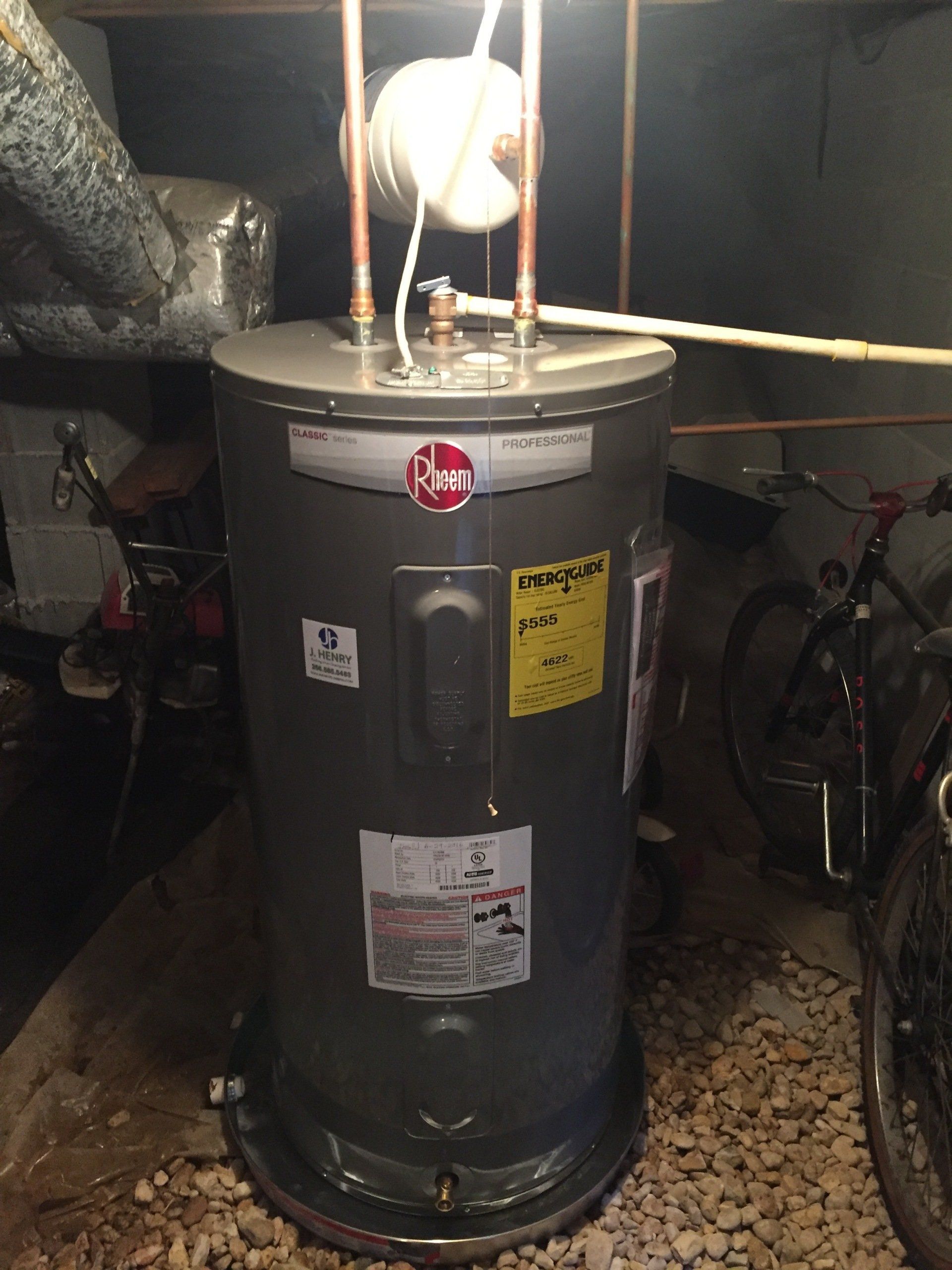 A water heater is sitting in a basement next to a bicycle.