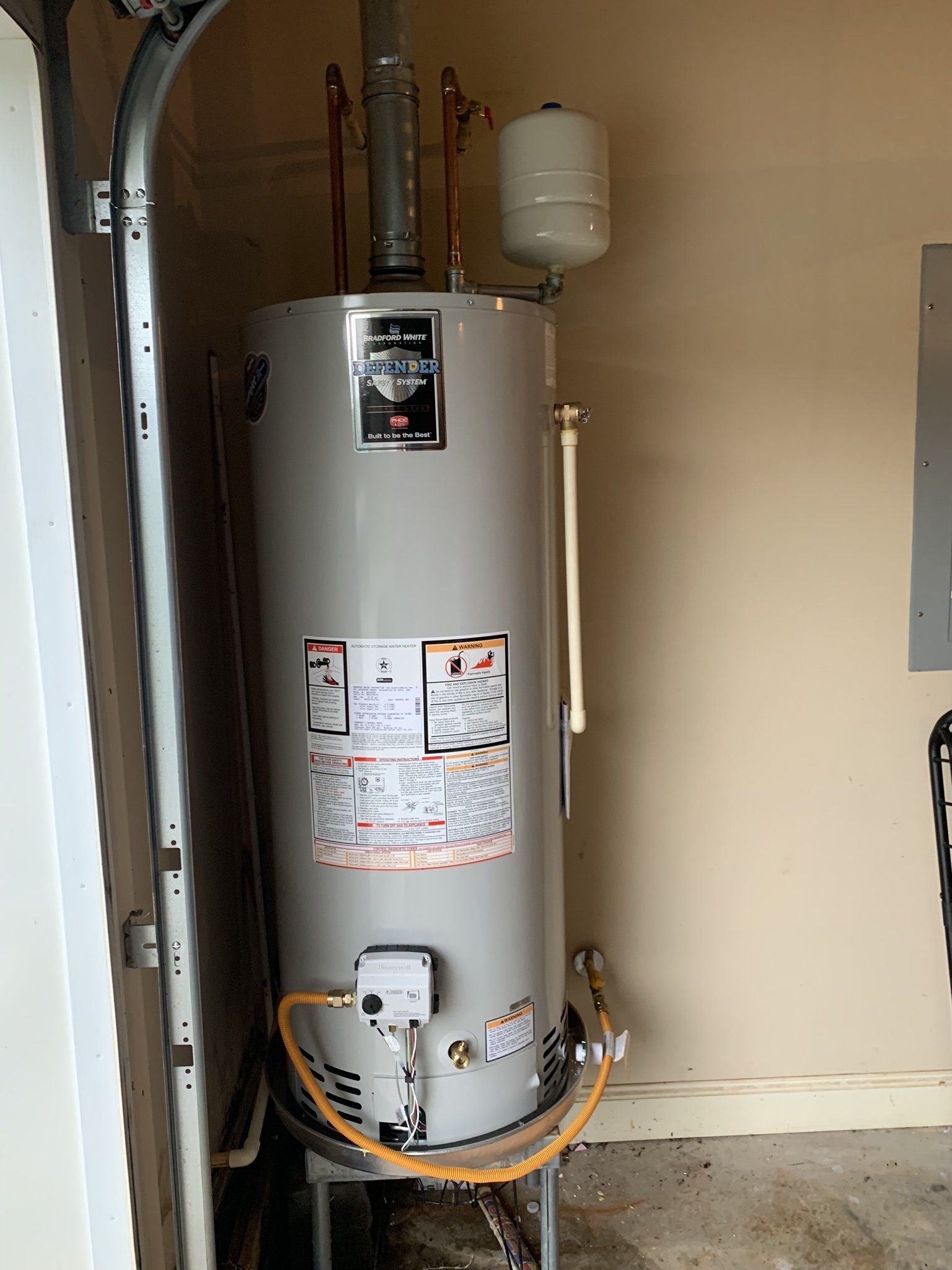 A water heater is sitting in a garage next to a garage door.