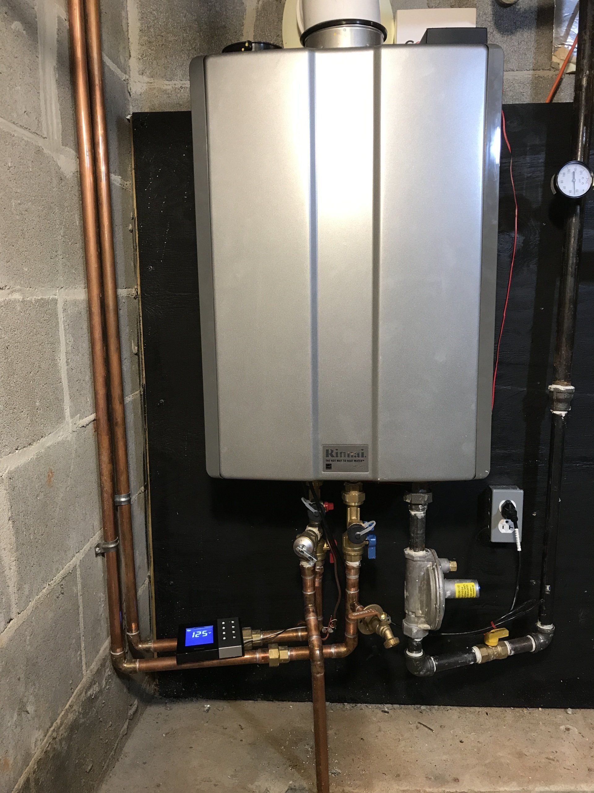 A stainless steel water heater is connected to copper pipes in a basement.