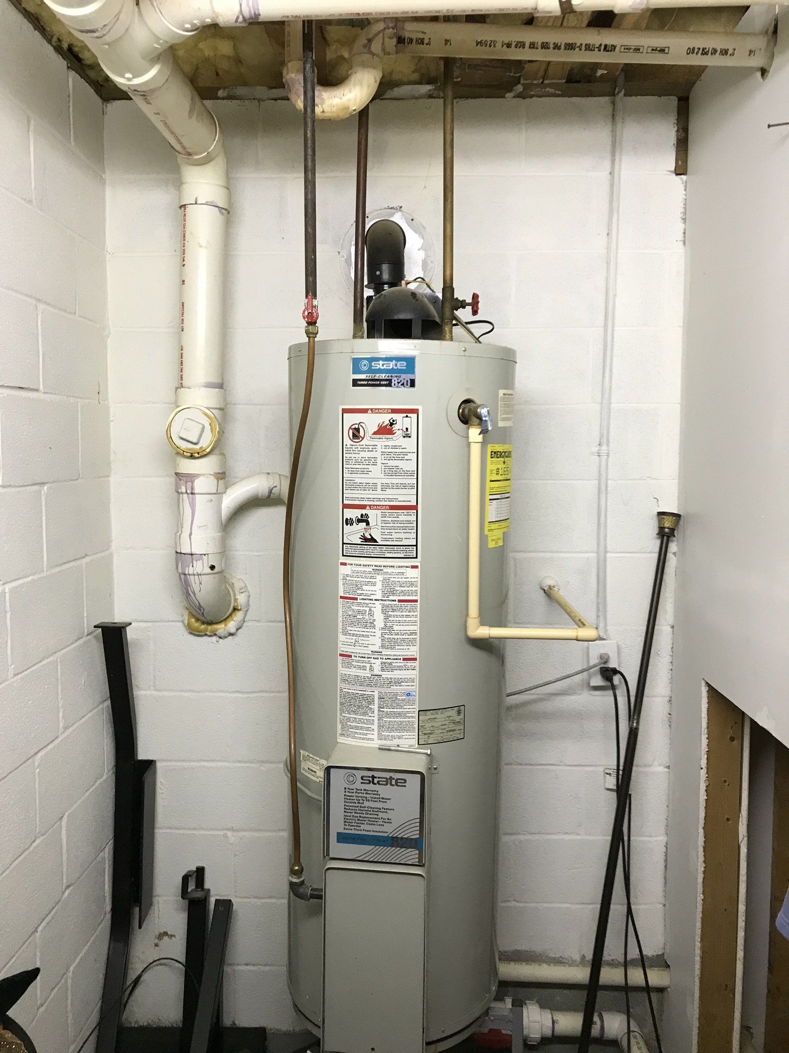 A water heater is sitting in a room next to a brick wall.