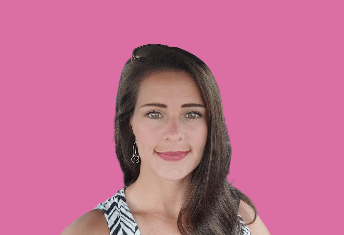 A woman is standing in front of a pink background and smiling.