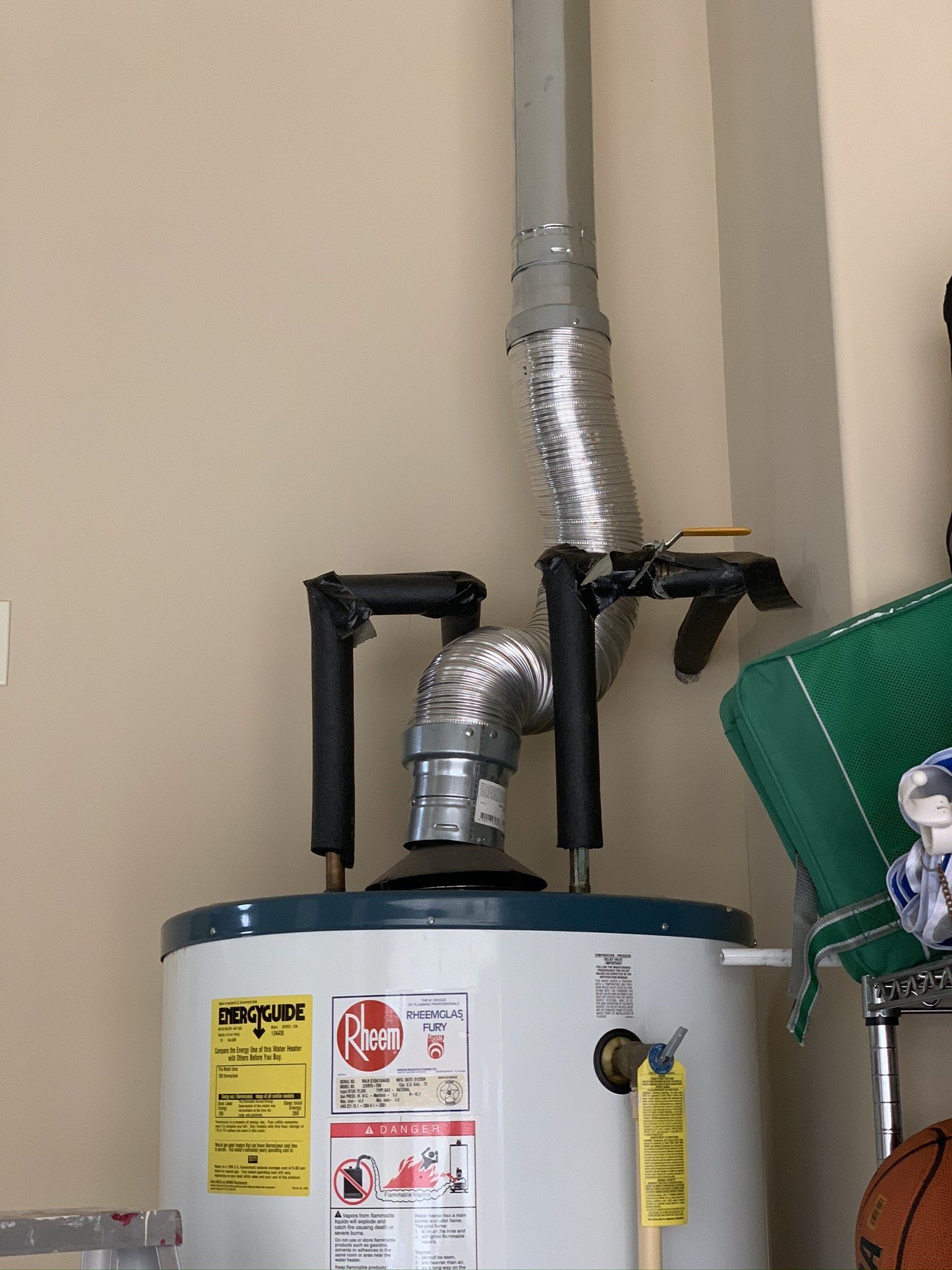 A white water heater is hanging on a wall next to a basketball.