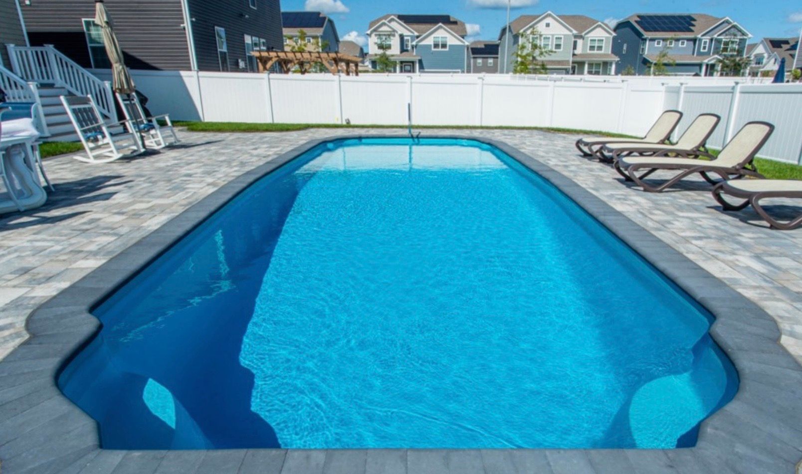 A large swimming pool surrounded by chairs and a white fence