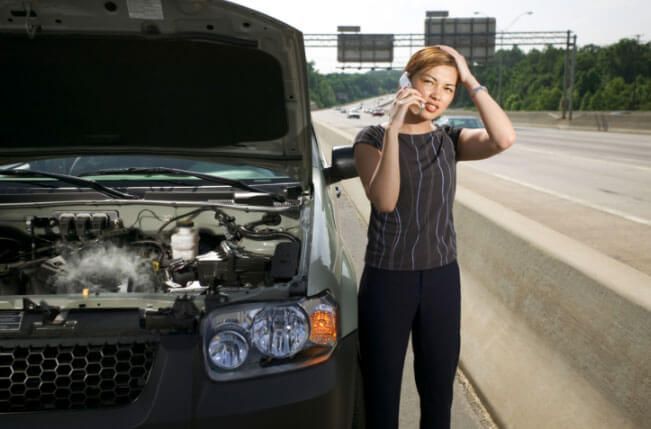 A woman is talking on a cell phone next to a broken down car.