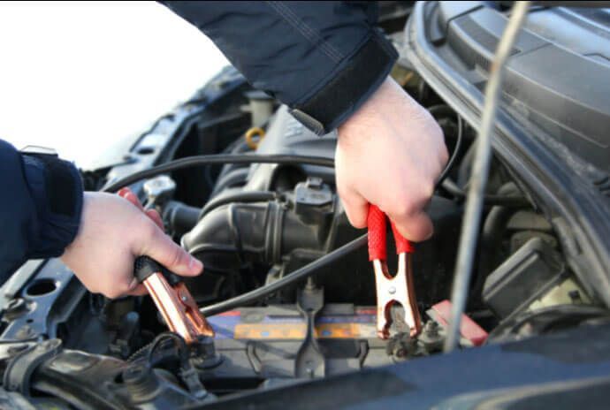 A person is charging a car battery with jumper cables.